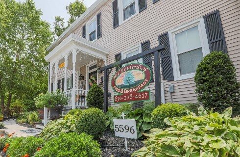 Outside of a large home with white portico over the door and large oval sign for a bed and breakfast