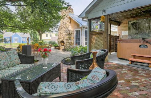 Outdoor patio with black wicker furniture , stone fireplace and hot tub under a roofed gazebo