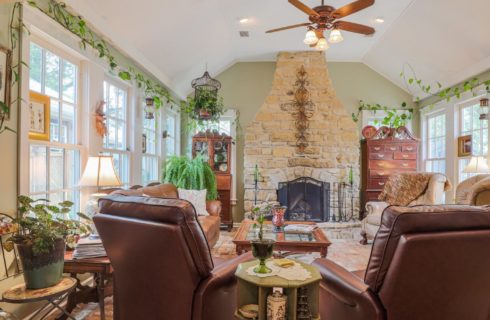 Cozy living room with large stone fireplace, greenery, large windows and leather furniture