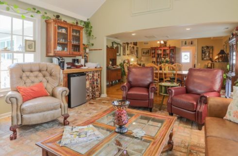 Living area of a home with leather chairs and small kitchenette overlooking a large dining room