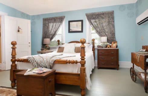 Bedroom with blue walls and queen bed in front of two windows with decorative drapery