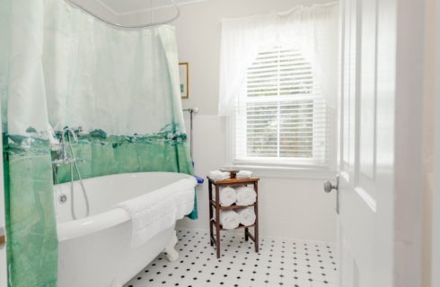 White bathroom with clawfoot tub surrounded by a green decorative shower curtain