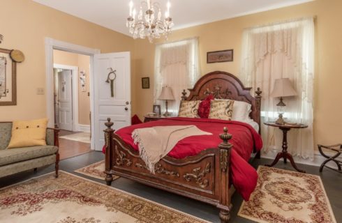 Bedroom with queen bed, antique headboard, sitting couch and oriental rugs