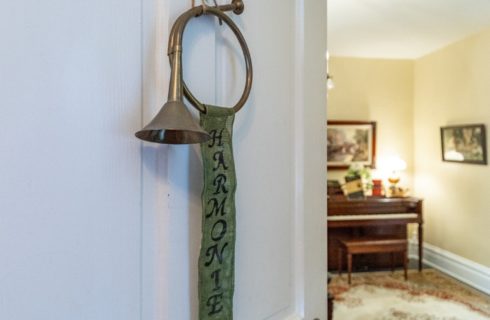 Antique horn with ribbon hanging on a white door open to a room with a piano