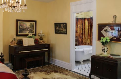 Bedroom with stand up piano, oriental rug and white clawfoot tub in the bathroom