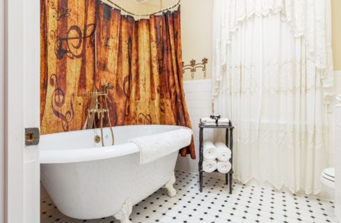 Bathroom with white clawfoot tub and window with lacy white curtain