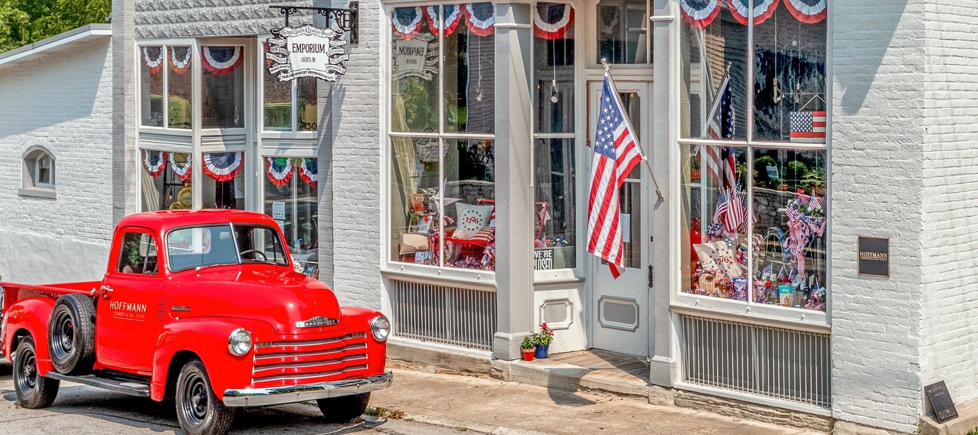 Bright red vintage pick up truck in front of a store with windows decked in Americana decor