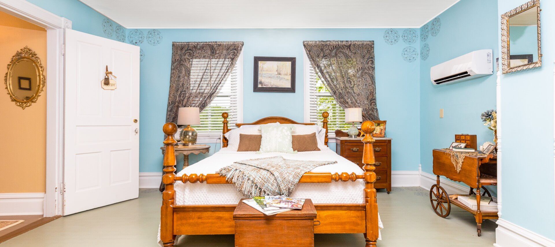 Bedroom with blue walls and queen bed in front of two windows with decorative drapery