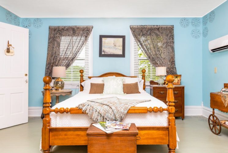 Bedroom with blue walls and queen bed in front of two windows with decorative drapery